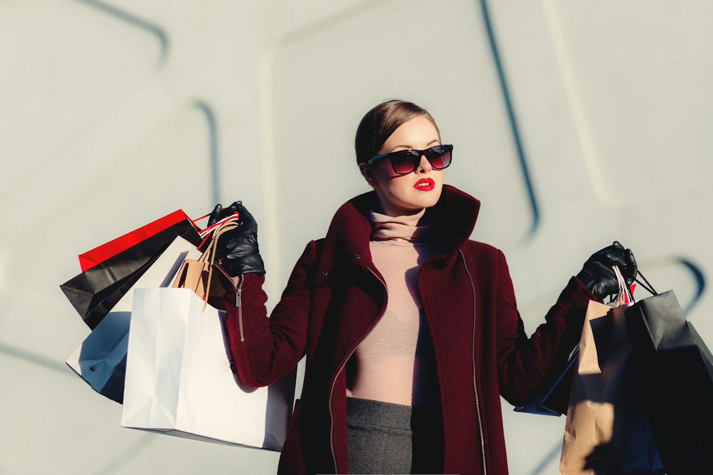Woman in sunglasses and an oxblood coat carrying shopping bags