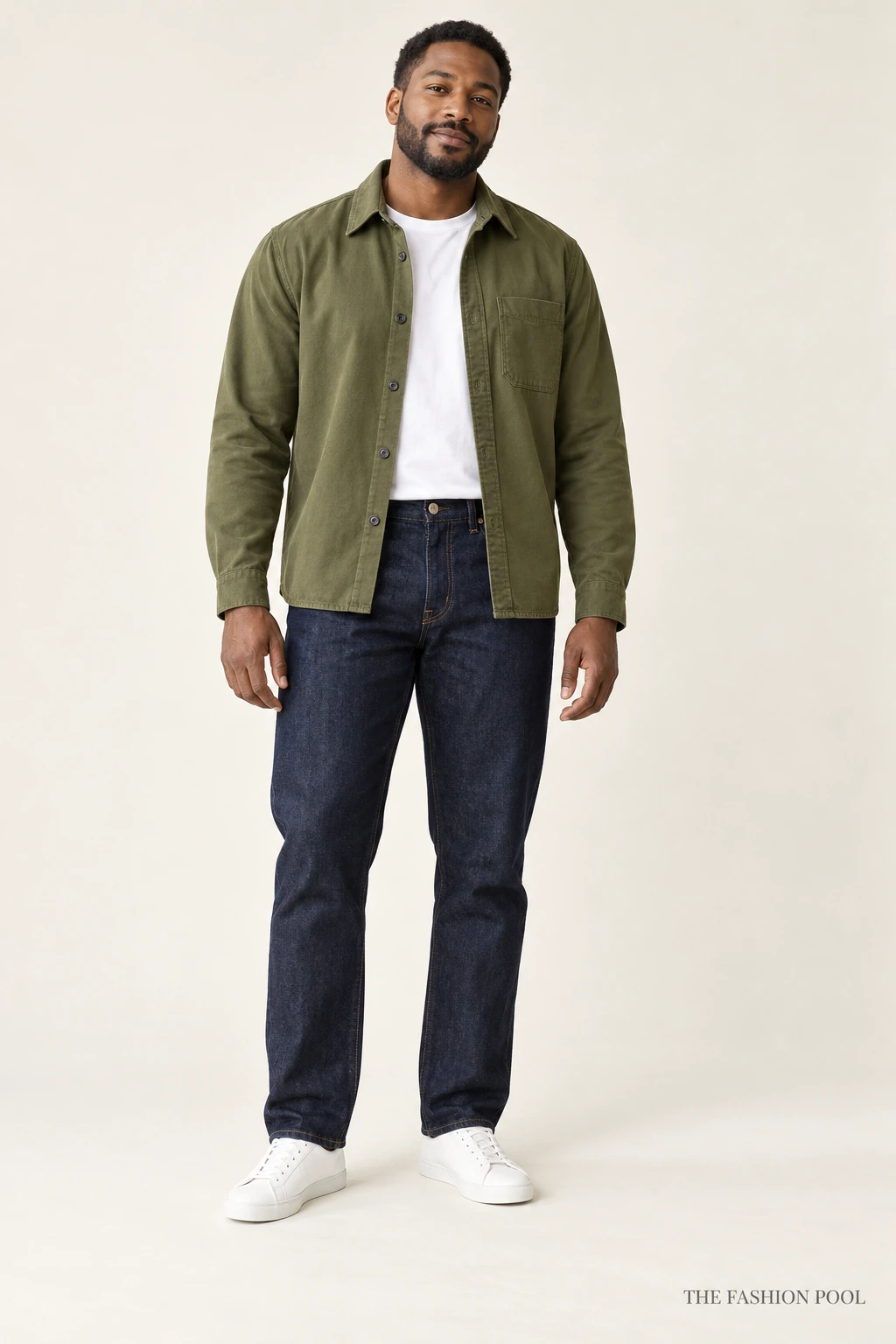 Man wearing an open olive overshirt over a white crew-neck tee with dark straight-leg jeans and white low-top sneakers.