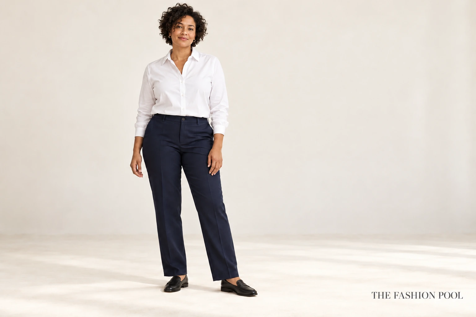 Woman wearing a comfortably buttoned white shirt with navy straight-leg trousers and black loafers.